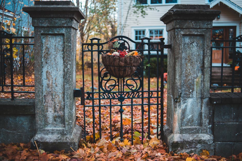 Stone gate adorned with autumn decorations, framed by fall foliage, leading to a traditional home.